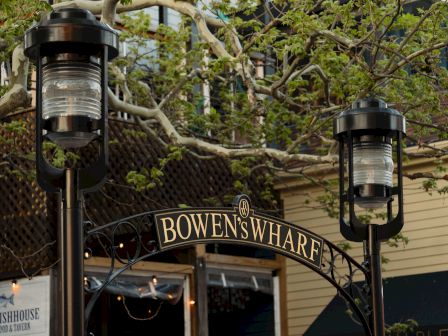 An outdoor entry with two lantern-style lights, leafy branches overhead, and a &ldquo;Bowen&rsquo;s Wharf&rdquo; sign in the background.