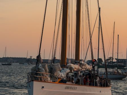 A sailboat named Adirondack IV sailing at sunset with crew on deck.