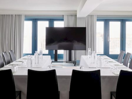 A modern conference room with a large screen, water bottles, glasses, and notepads arranged on tables forming a U-shape.