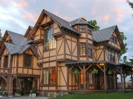 A large Tudor-style house with steep gables and stone accents under a colorful sunset sky.