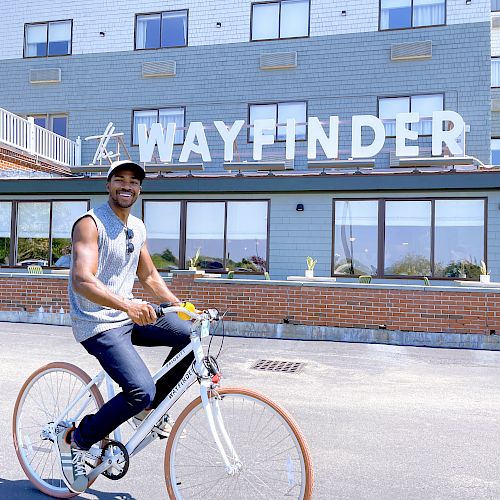 A person is riding a bicycle in front of a building with a sign that reads 