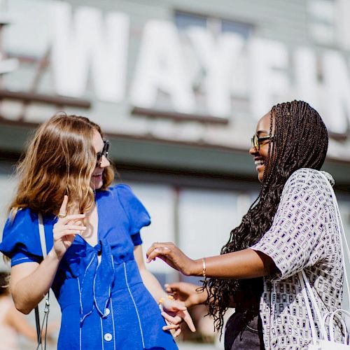 Two women are laughing and enjoying themselves in front of a sign that reads 