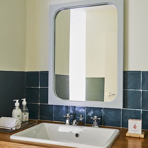 A bathroom sink with a wooden countertop, a large mirror, two soap dispensers, and a small framed picture, beneath overhead lighting.