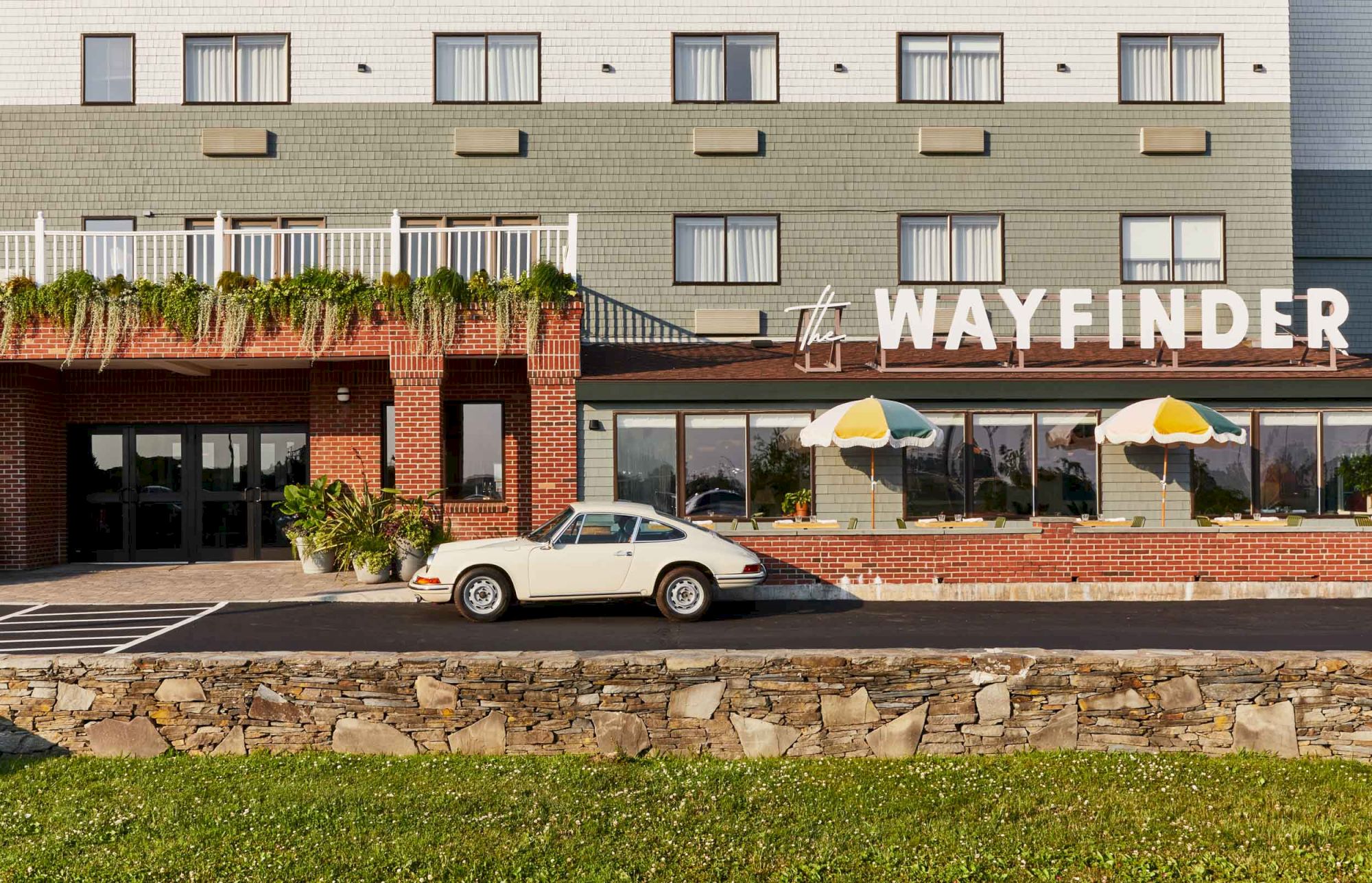 A white vintage car parked in front of a brick storefront with awnings; a building labeled &ldquo;WAYFINDER&rdquo; behind it.