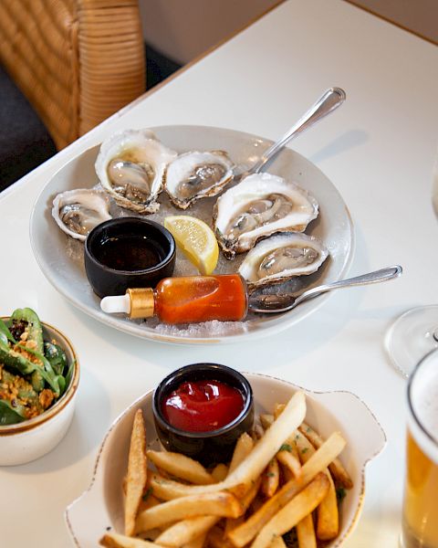 Plate of fresh oysters with lemon, cocktail sauce, chili mignonette, fries, salad, and a cold beer.