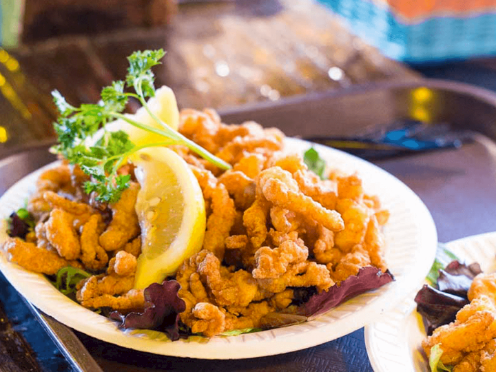 A plate of crispy fried chicken bites topped with fresh parsley and lemon wedges, with chips in the background.