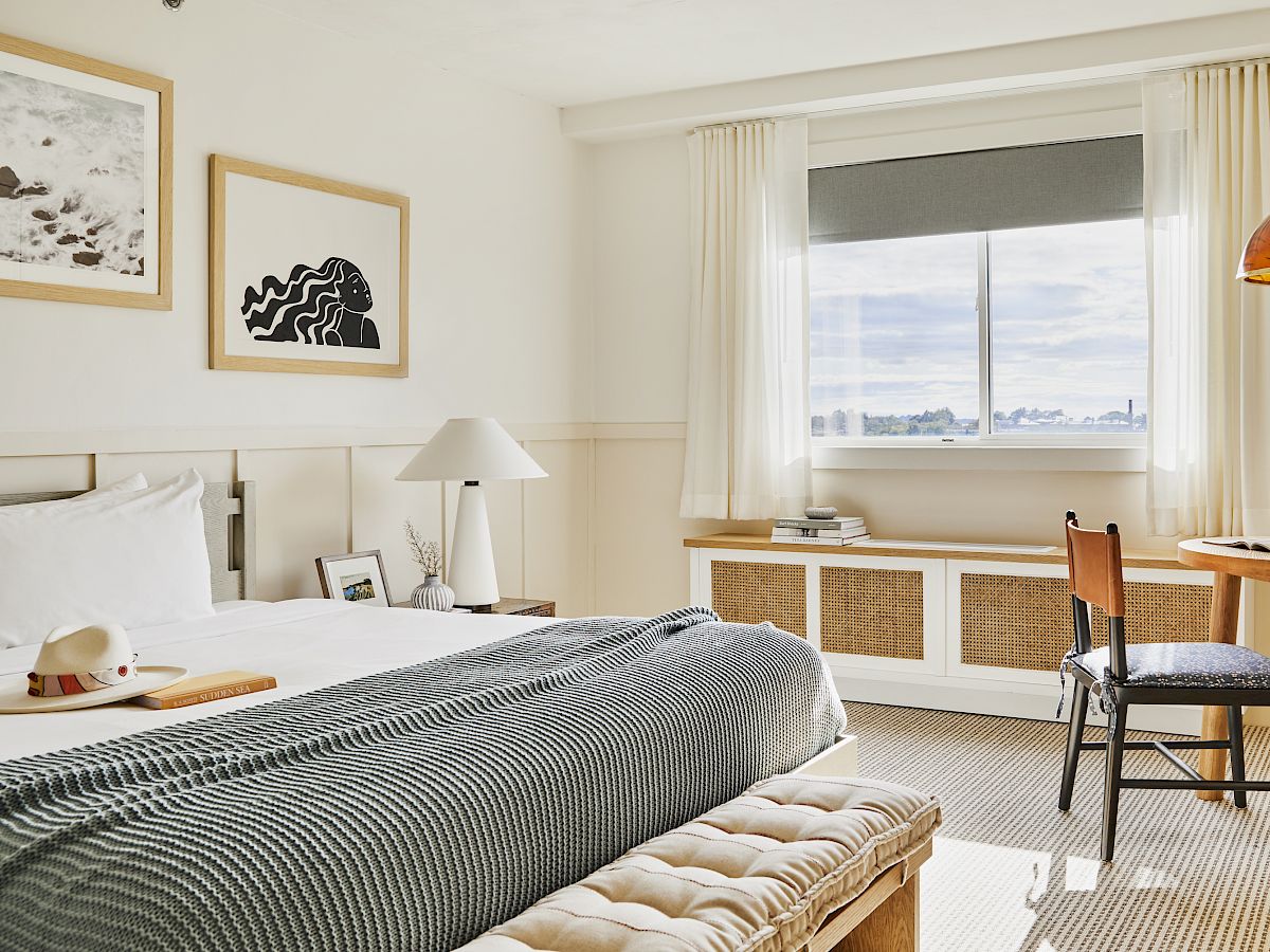 A cozy bedroom with a neatly made bed, artwork on the walls, and a window offering a scenic view.