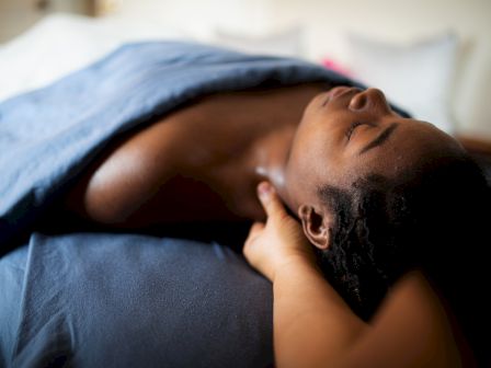 A person is lying on a massage table, covered with a blue sheet, receiving a neck and shoulder massage.