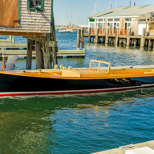 A bright yellow motorboat is moored at a wooden marina pier beside harbor buildings and calm blue water.