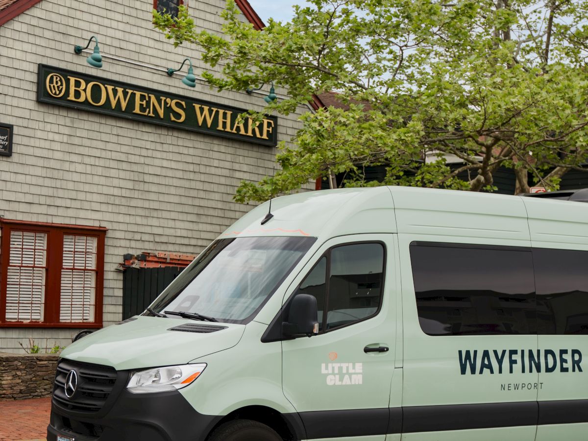 A green delivery truck sits in front of a building sign reading &ldquo;Bowen&rsquo;s Wharf&rdquo; as trees leaf out overhead.