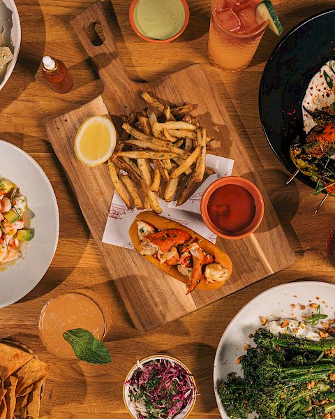 A table spread with fries, salads, sandwiches, grilled plates, dipping sauces, and drinks for a full meal.