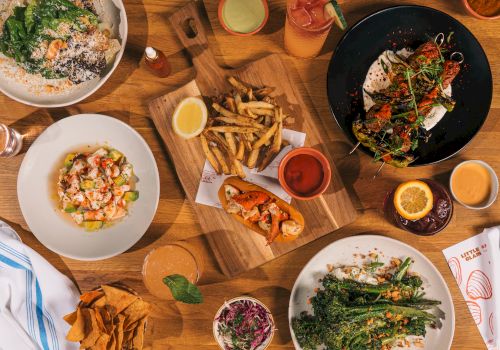 A table spread with fries, salads, sandwiches, grilled plates, dipping sauces, and drinks for a full meal.