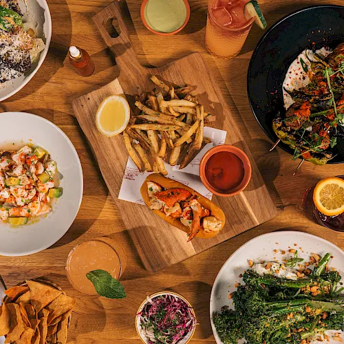 A table spread with fries, salads, sandwiches, grilled plates, dipping sauces, and drinks for a full meal.