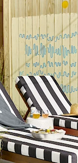 The image shows two black and white striped lounge chairs beside a pool, with drinks, a hat, and towels, set against a wooden fence.