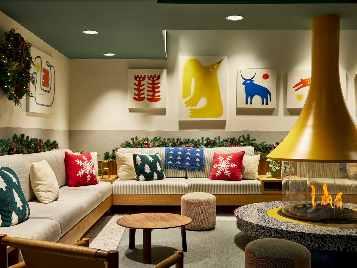 A cozy lounge decorated for Christmas&mdash;sofa, pillows, garlands, colorful animal wall art, and a lit fireplace glow everywhere.