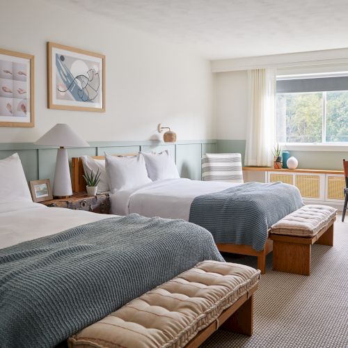 A bright, cozy bedroom and study area with a bed, nightstands, colorful decor, and a workstation by the window.