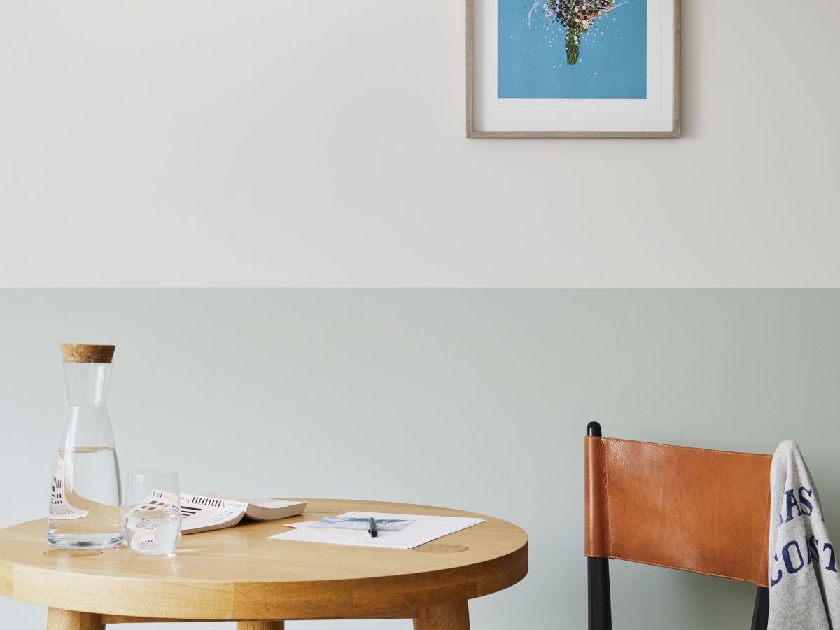 A wooden table with a water carafe, a chair with a blanket, a hanging lamp, and a framed artwork on the wall.