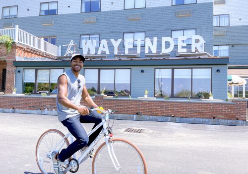 A person is riding a bicycle in front of a building with a sign that reads 