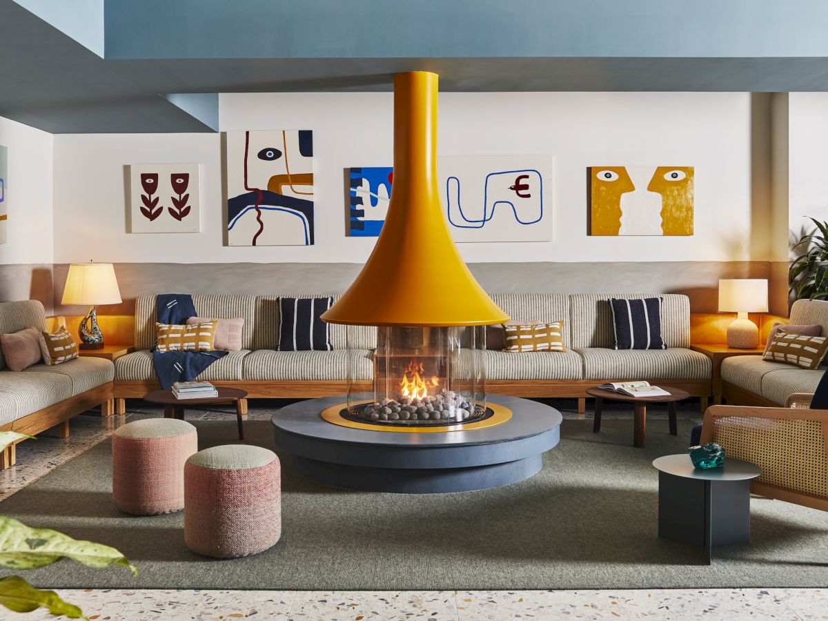 A modern living room with a central yellow fireplace, abstract art, comfy seating, and ambient lighting creates a warm atmosphere.