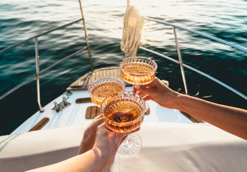 Three people are toasting with glasses on a boat, overlooking water in a serene setting.