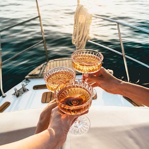 Three people are toasting with glasses on a boat, overlooking water in a serene setting.