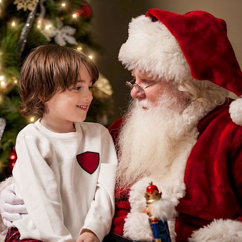 A child sitting with Santa Claus near a decorated Christmas tree, sharing a joyful moment.