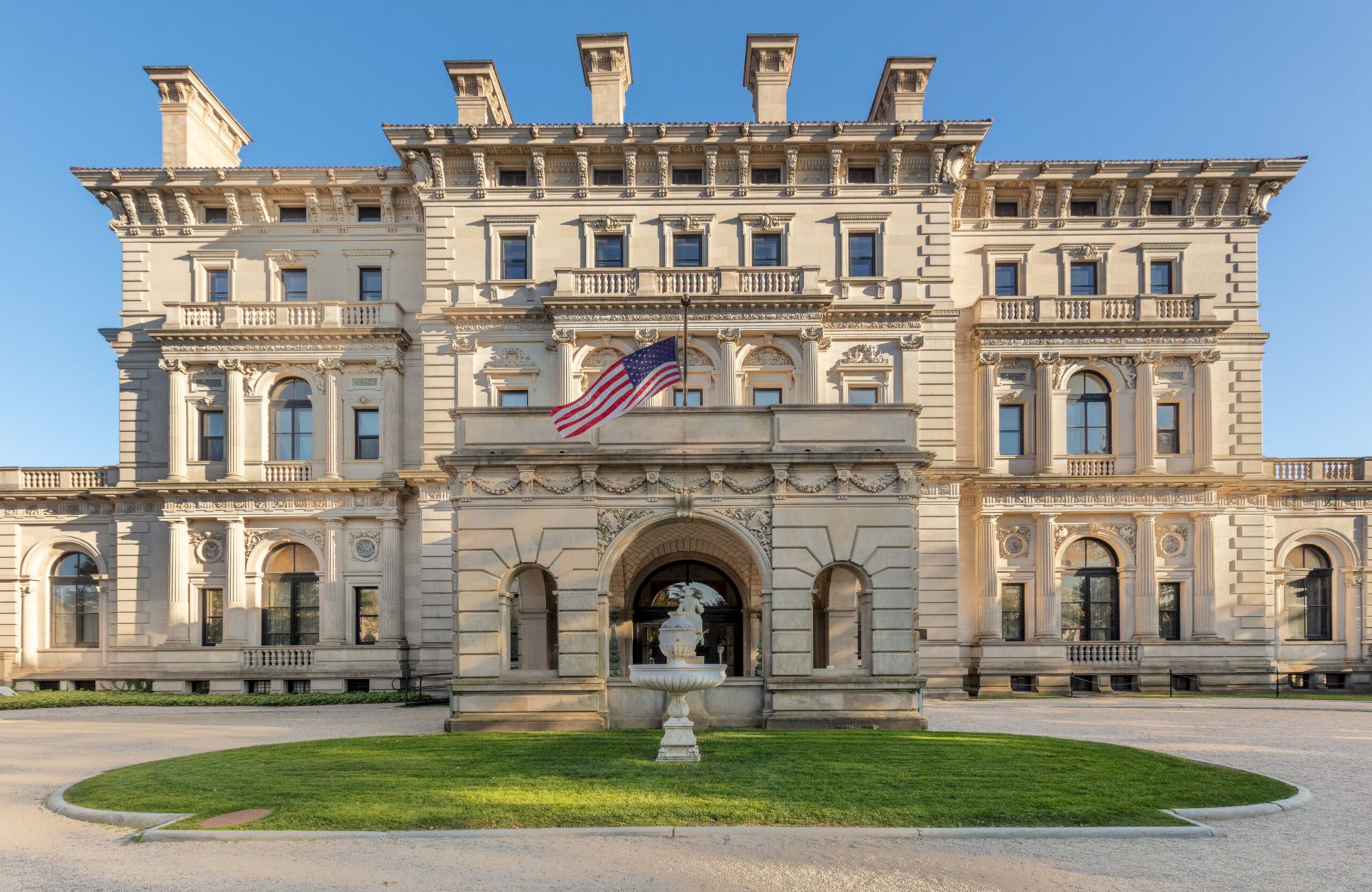 A grand, ornate mansion with a central American flag and a front lawn under a clear blue sky.