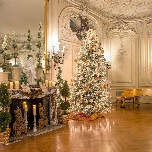 Elegantly decorated room with a lit Christmas tree, ornate fireplace, candles, greenery, and a grand piano in a luxurious setting.