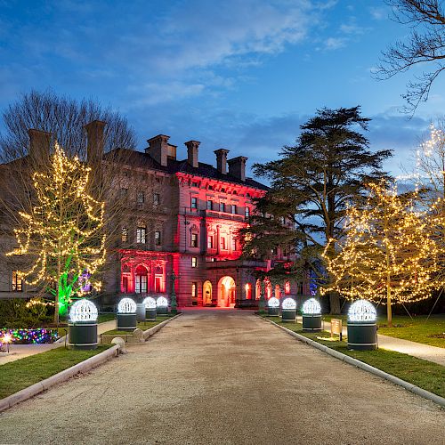 A grand building beautifully lit with colorful lights, surrounded by decorated trees along a pathway, creating a festive atmosphere.