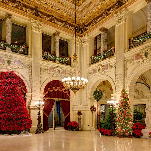 A grand hall decorated for Christmas with elaborate decorations, red ornamental trees, and classical architecture.