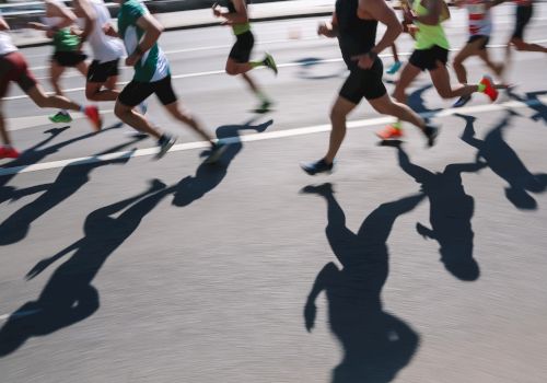 The image shows a group of runners in motion with their shadows cast on the pavement during a race or marathon.