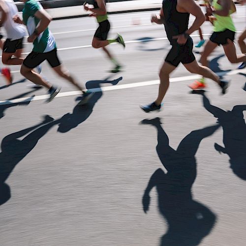 The image shows a group of runners in motion with their shadows cast on the pavement during a race or marathon.