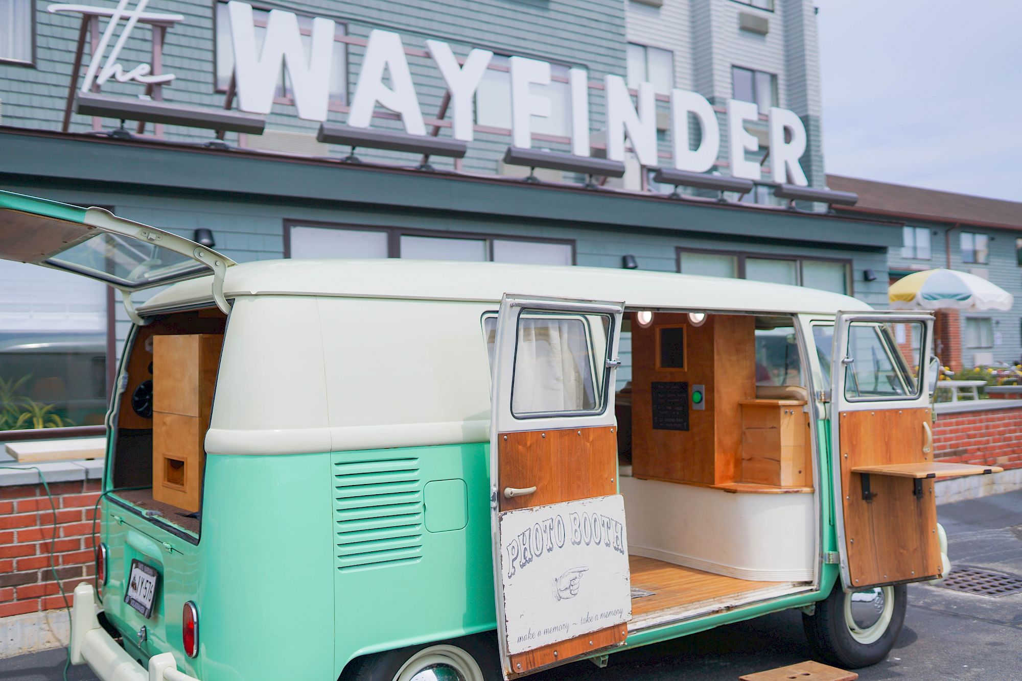 A vintage mint green van with open doors is parked in front of a building with "The Wayfinder" sign.