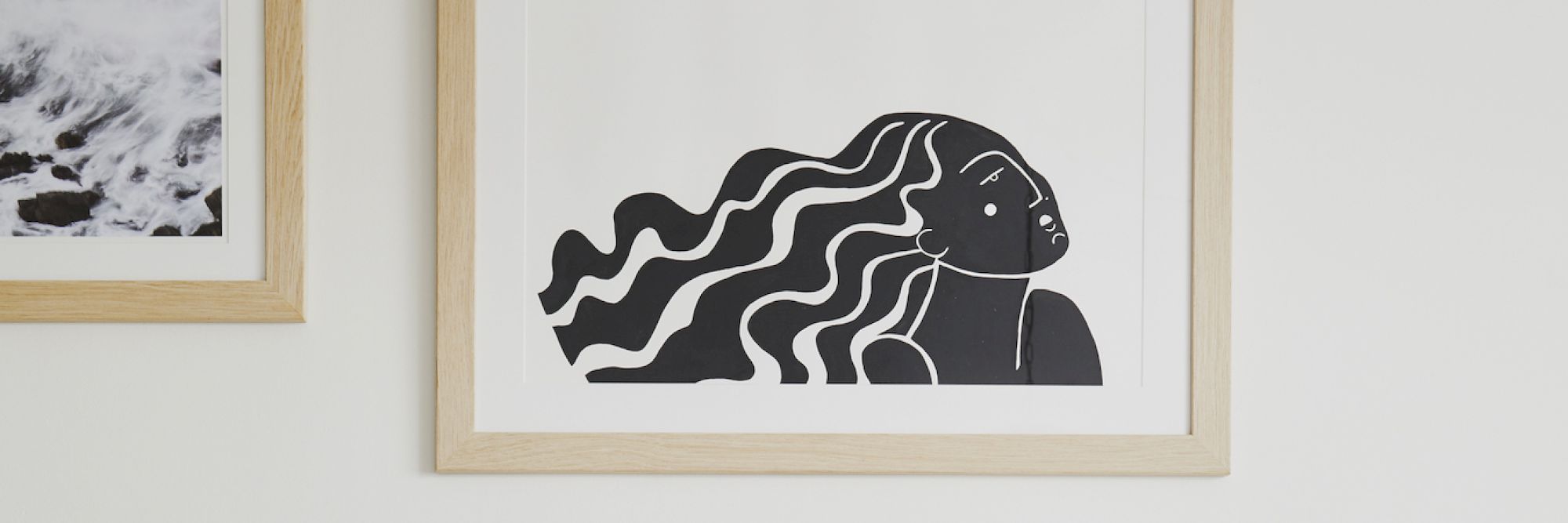 The image shows two framed artworks: one with waves crashing on rocks, another with a stylized drawing of a person with long, flowing hair.