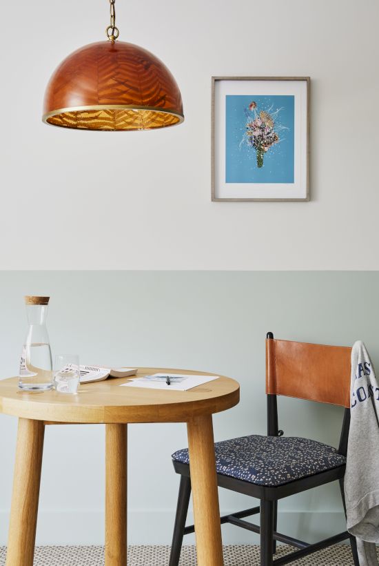 The image shows a wooden table with a jug and papers, a chair with a cloth, a pendant lamp, and a framed artwork on the wall.