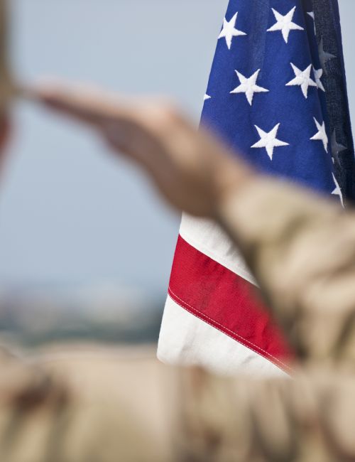 A person in military uniform saluting the American flag, with a blurred background.