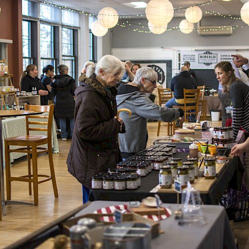 People browsing products at an indoor market with lanterns hanging from the ceiling, and tables displaying various items for sale.