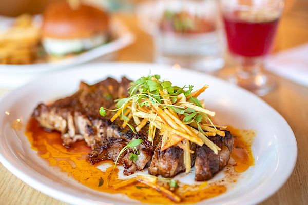 A plate of grilled steak with vegetables, a burger with fries, a drink, and a water bottle are on a table.