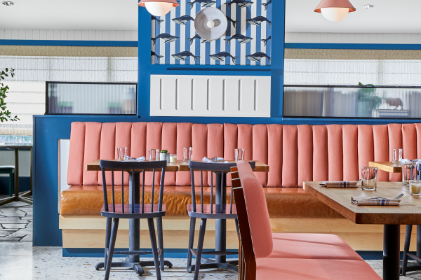Restaurant interior with pink and orange seating, blue accents, pendant lights, and wooden furnishings.