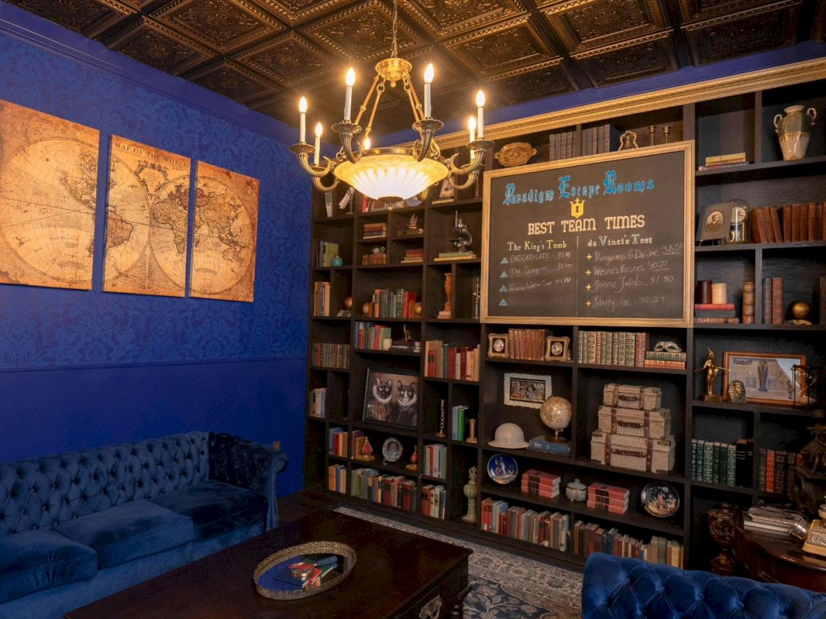 A cozy library with blue walls, vintage chandelier, maps, bookshelves, and plush seating, creating an inviting atmosphere.