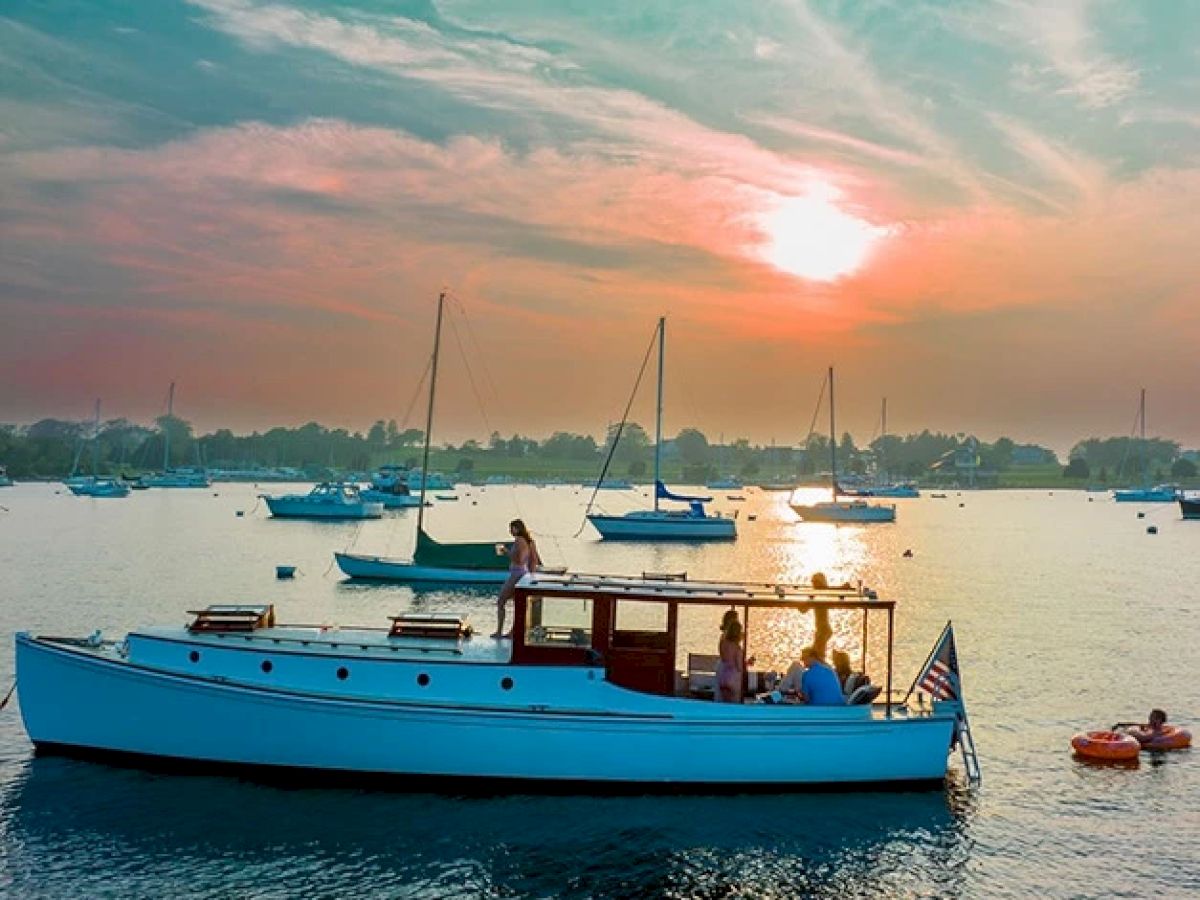 A serene sunset scene with several boats on a calm lake, with people enjoying a ride on the main white boat in the foreground.