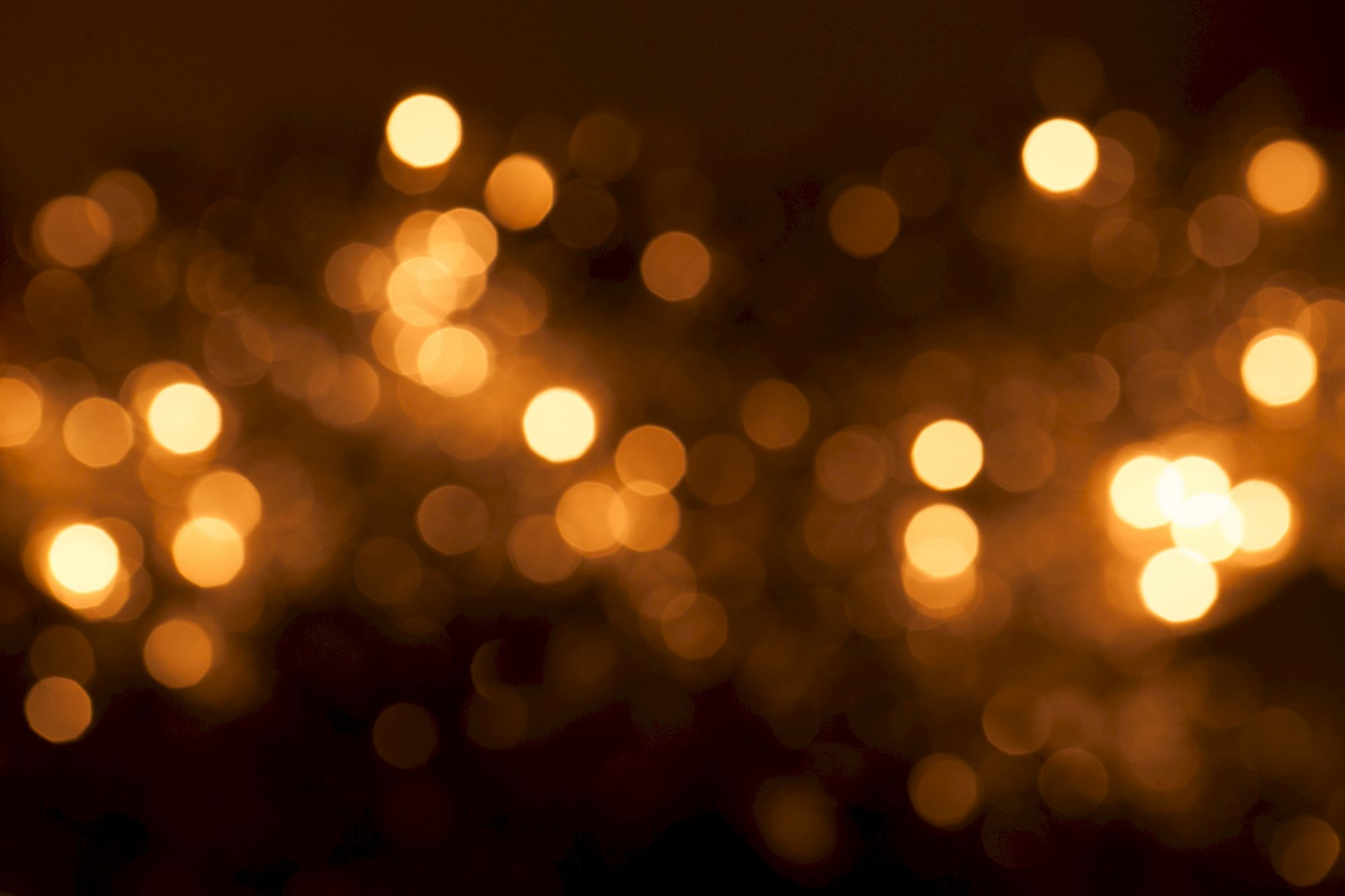 A blurred image of warm, golden bokeh lights creating an abstract pattern against a dark background.