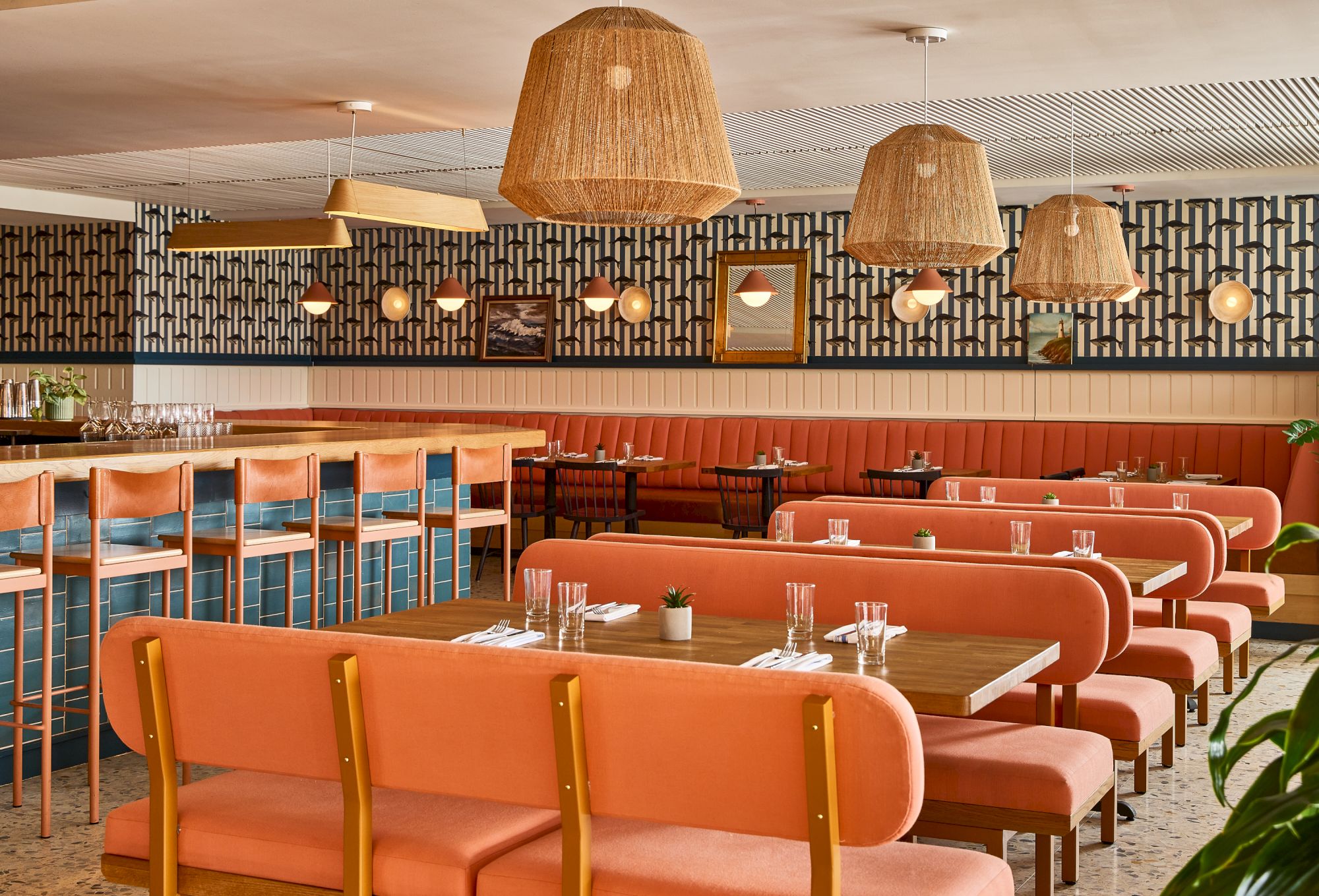 Colorful retro diner seating with pink booths, wooden chairs, hanging lamps, and a long bar counter in a cozy, patterned spaceending sentence.