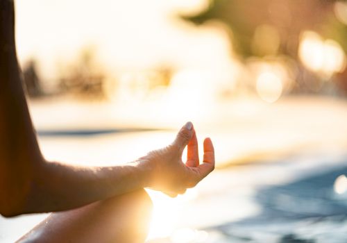 A person is meditating outdoors with a focused hand gesture, surrounded by a bright, blurred background in warm sunlight.