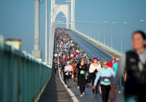 A large group of people is participating in a walking or running event on a bridge under clear skies.