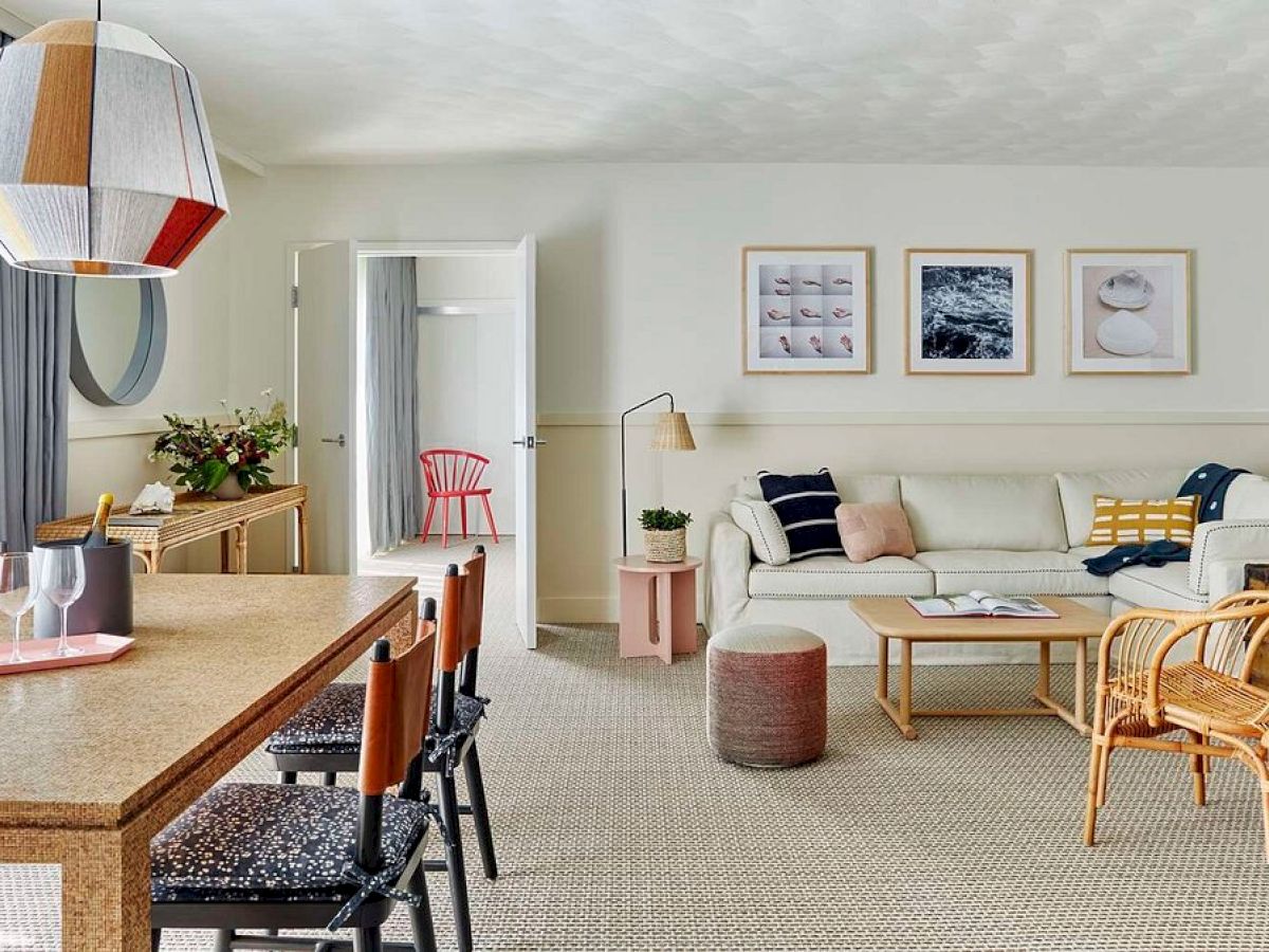 A modern living room with a cozy sofa, colorful chairs, framed art, and a stylish dining area with a geometric pendant lamp.