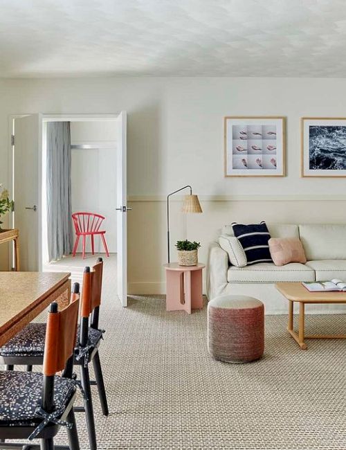 A modern living room with a cozy sofa, colorful chairs, framed art, and a stylish dining area with a geometric pendant lamp.
