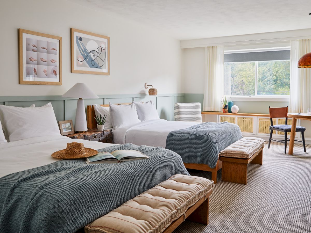 A cozy bedroom features two beds, art on the walls, a window, and a seating area with a table and chairs for relaxation.