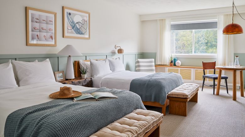 A cozy bedroom features two beds, art on the walls, a window, and a seating area with a table and chairs for relaxation.
