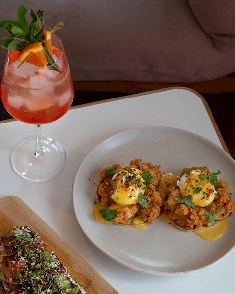 A bright cocktail with mint, and two plates of tapas on a white table&mdash;one with topped crostini and the other with mini bruschetta slices.